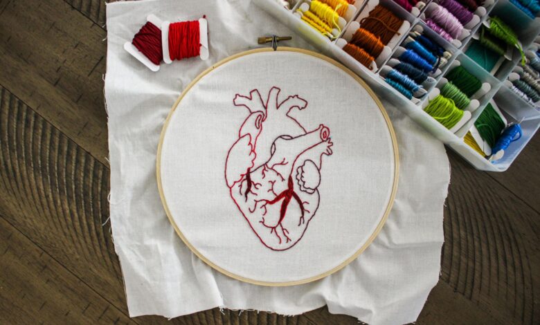 Close-up of an anatomical heart embroidery with vibrant threads on a wooden table.