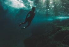 Silhouette of a diver exploring deep underwater surrounded by sunlight rays.