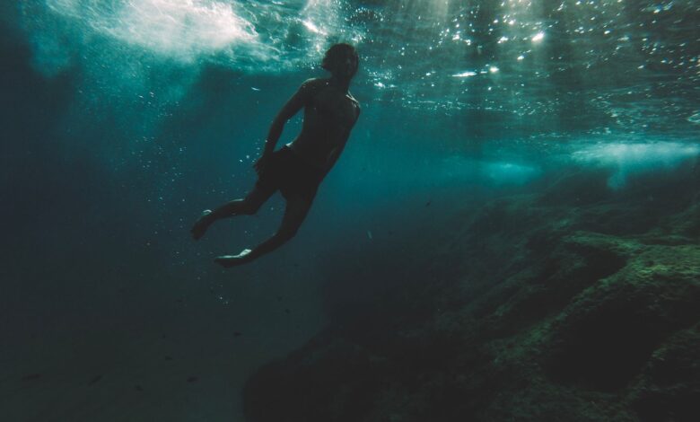 Silhouette of a diver exploring deep underwater surrounded by sunlight rays.