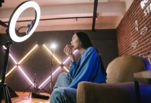 Asian woman content creator eating pizza while recording a video indoors with ring light.