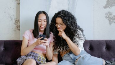 Two teenage girls happily sharing a moment on a sofa while looking at a smartphone indoors.