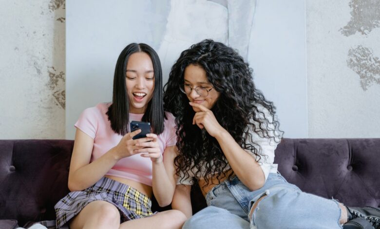 Two teenage girls happily sharing a moment on a sofa while looking at a smartphone indoors.