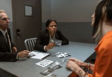 Interrogation scene with detectives questioning a handcuffed suspect inside a jail room.
