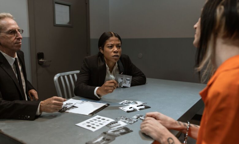 Interrogation scene with detectives questioning a handcuffed suspect inside a jail room.