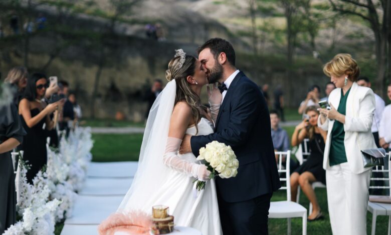 A newlywed couple shares a romantic kiss during an outdoor wedding ceremony.
