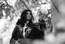 Black and white portrait of a man in costume holding a skull in an outdoor setting.