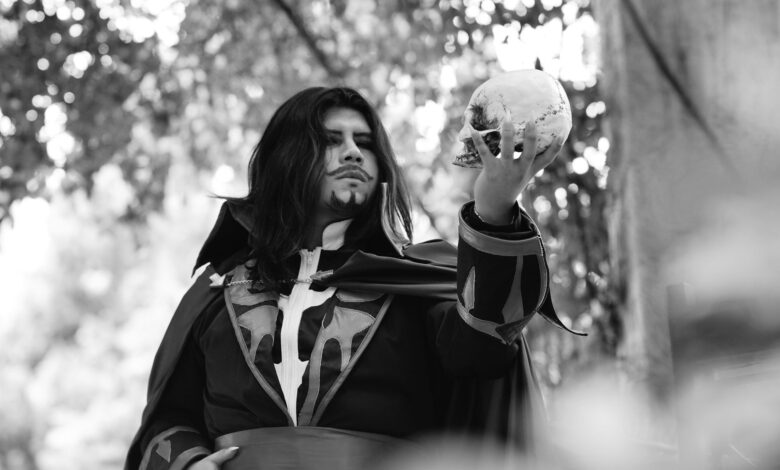 Black and white portrait of a man in costume holding a skull in an outdoor setting.
