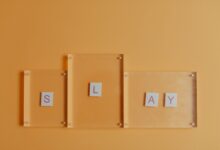 Artistic arrangement of letters spelling 'Slay' with glass frames on a vibrant orange backdrop.