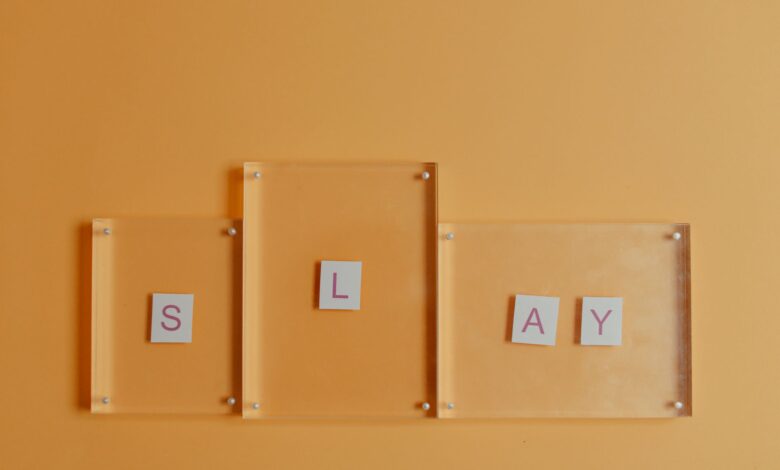 Artistic arrangement of letters spelling 'Slay' with glass frames on a vibrant orange backdrop.