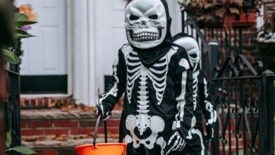 Anonymous kids with buckets wearing skeleton costumes and masks standing on terrace near entrance of house during trick or treat game