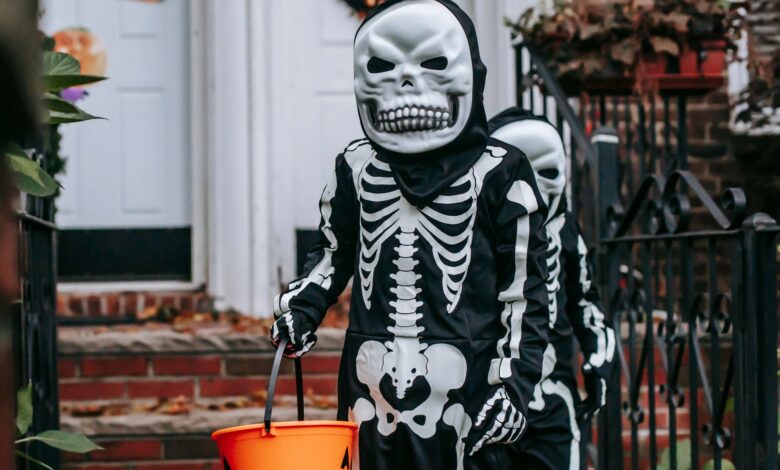 Anonymous kids with buckets wearing skeleton costumes and masks standing on terrace near entrance of house during trick or treat game