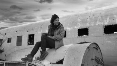 Black and white photo of a woman sitting on an abandoned plane in Iceland under a cloudy sky.