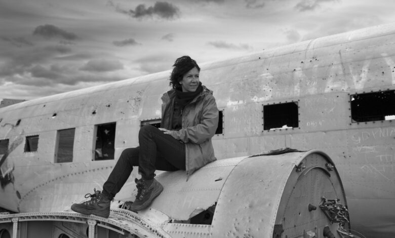 Black and white photo of a woman sitting on an abandoned plane in Iceland under a cloudy sky.