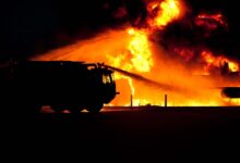 Dramatic image of a fire truck silhouette against a massive blaze, showcasing emergency response.