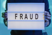 Close-up of hands holding a sign with 'fraud', illuminated in blue light.