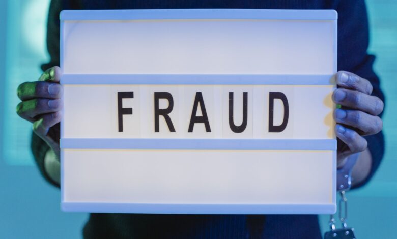 Close-up of hands holding a sign with 'fraud', illuminated in blue light.