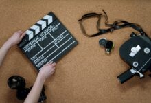 Top view of classic filmmaking tools including a slate and vintage camera on a cork surface.