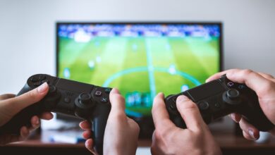 Close-up of hands holding gaming controllers in front of a TV. Engaged in a video gaming session.