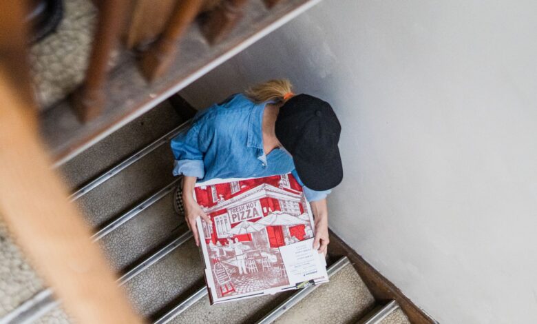 Overhead view of woman delivering pizza on stairs, highlighting delivery work.
