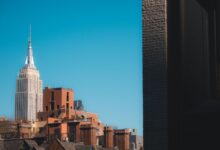 Capture of the Empire State Building peeking over New York rooftops against a clear blue sky.