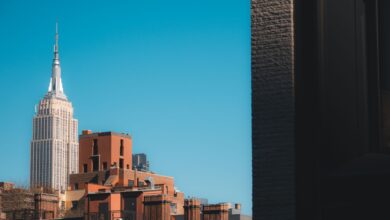 Capture of the Empire State Building peeking over New York rooftops against a clear blue sky.