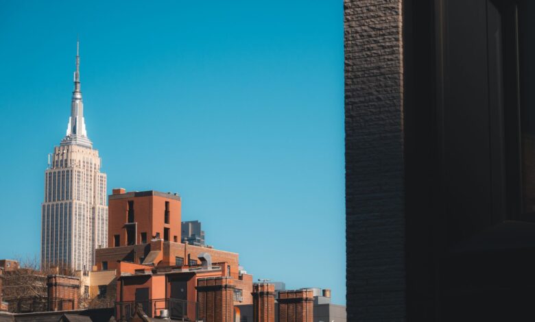 Capture of the Empire State Building peeking over New York rooftops against a clear blue sky.