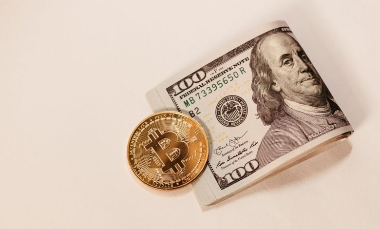A Bitcoin coin placed next to a rolled US hundred dollar bill, symbolizing cryptocurrency and traditional currency.