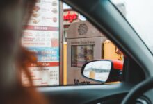 Blurred driver choosing food from menu and telling order to drive thru speaker post