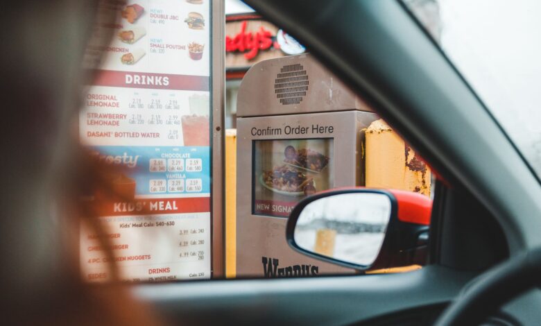 Blurred driver choosing food from menu and telling order to drive thru speaker post
