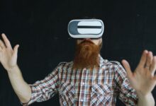 Bearded man in plaid shirt using virtual reality headset indoors, immersed in VR experience.