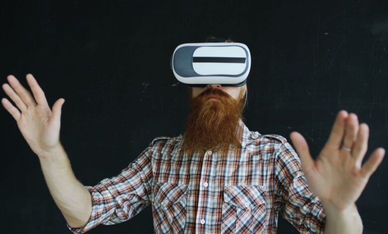 Bearded man in plaid shirt using virtual reality headset indoors, immersed in VR experience.