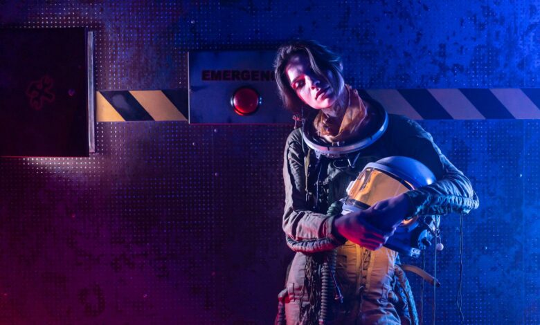 Portrait of a woman in a space suit in a dark, futuristic setting with dramatic lighting.