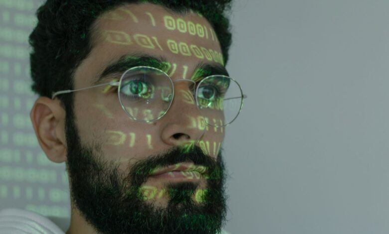 A bearded man with digital binary code projected on his face, symbolizing cybersecurity and technology.