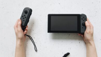 Close-up of hands holding a Nintendo Switch and Joy-Con controllers on a white surface.