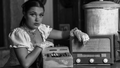 Black and white portrait of a woman in vintage attire, posing with an antique radio and typewriter.