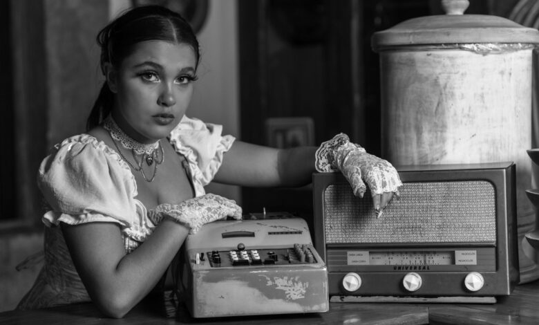 Black and white portrait of a woman in vintage attire, posing with an antique radio and typewriter.