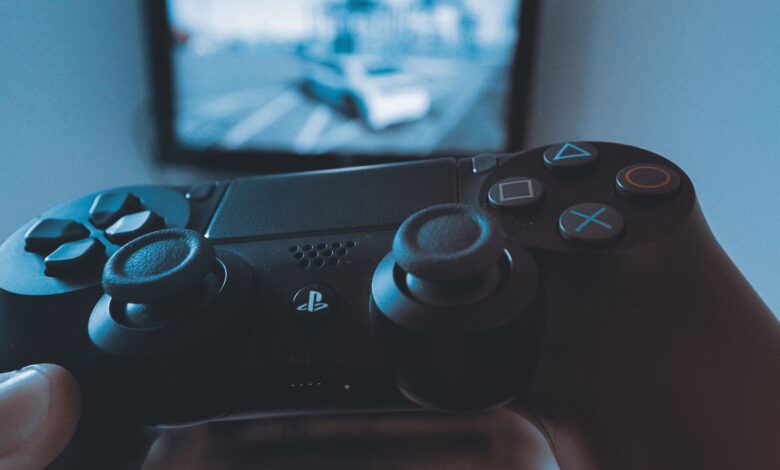 A hand holding a wireless game controller in front of a blurry screen, capturing the gaming experience.