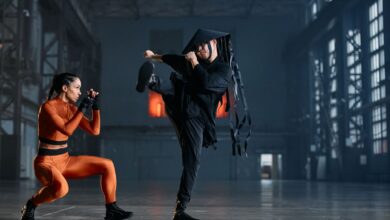 Two cosplayers performing martial arts poses in an industrial space, showcasing vibrant costumes and action.