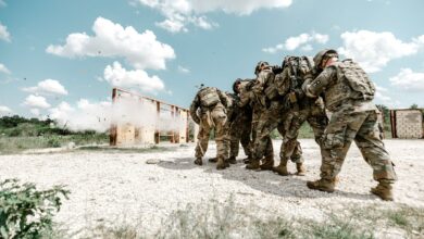 Group of soldiers in military uniforms performing a training exercise outdoors with explosive simulation.