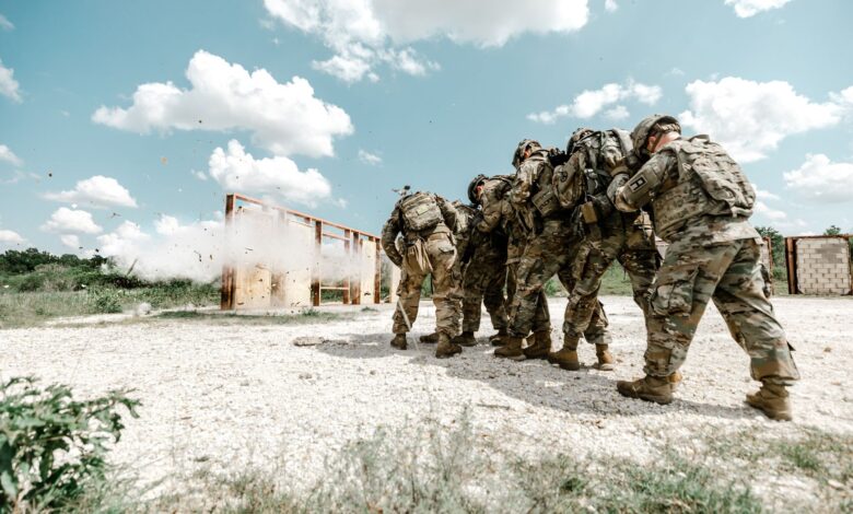 Group of soldiers in military uniforms performing a training exercise outdoors with explosive simulation.