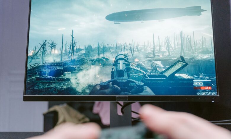 A person playing a video game on a high-resolution monitor, showcasing a war-themed landscape.