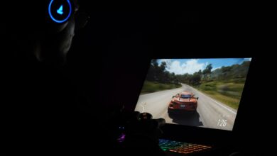 A gamer using a laptop and headphones to play a car racing game in a dark setting.