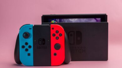 Close-up of Nintendo Switch console with red and blue Joy-Con controllers on pink background.
