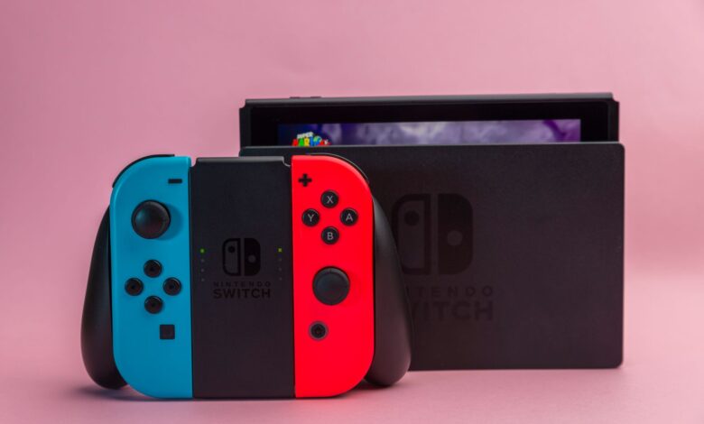 Close-up of Nintendo Switch console with red and blue Joy-Con controllers on pink background.