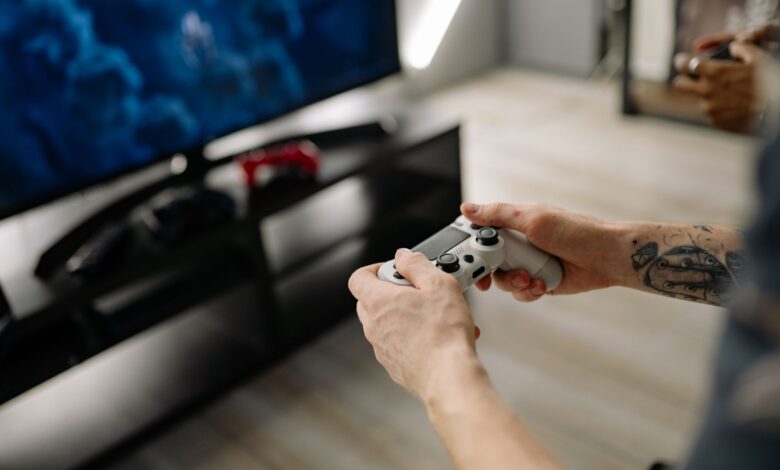 Person playing video games using a game controller indoors on a modern TV setup.