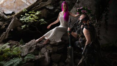 A woman in white and a sci-fi armored figure in a post-apocalyptic setting with ruins.