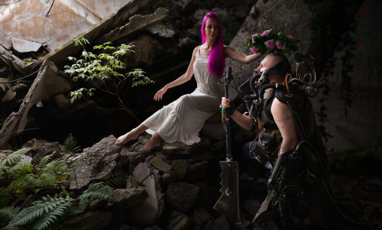 A woman in white and a sci-fi armored figure in a post-apocalyptic setting with ruins.