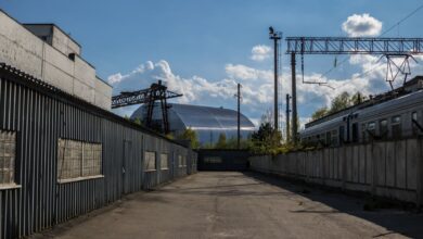 View of Chernobyl's new safe confinement and railway tracks under a blue sky.