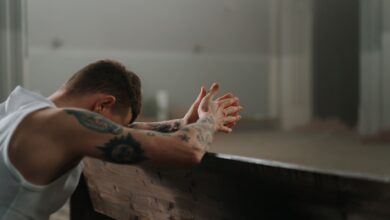 A tattooed man is solemnly praying indoors, reflecting spirituality and repentance.