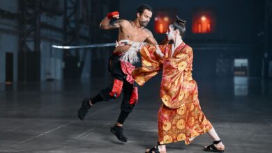 A dynamic martial arts cosplay scene featuring a kimono-clad fighter and a tattooed fighter in motion, indoors.